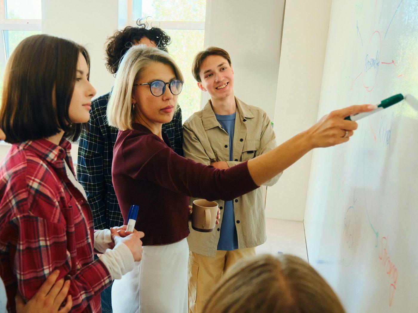 A team gathered round a whiteboard as a colleague points to a diagram
